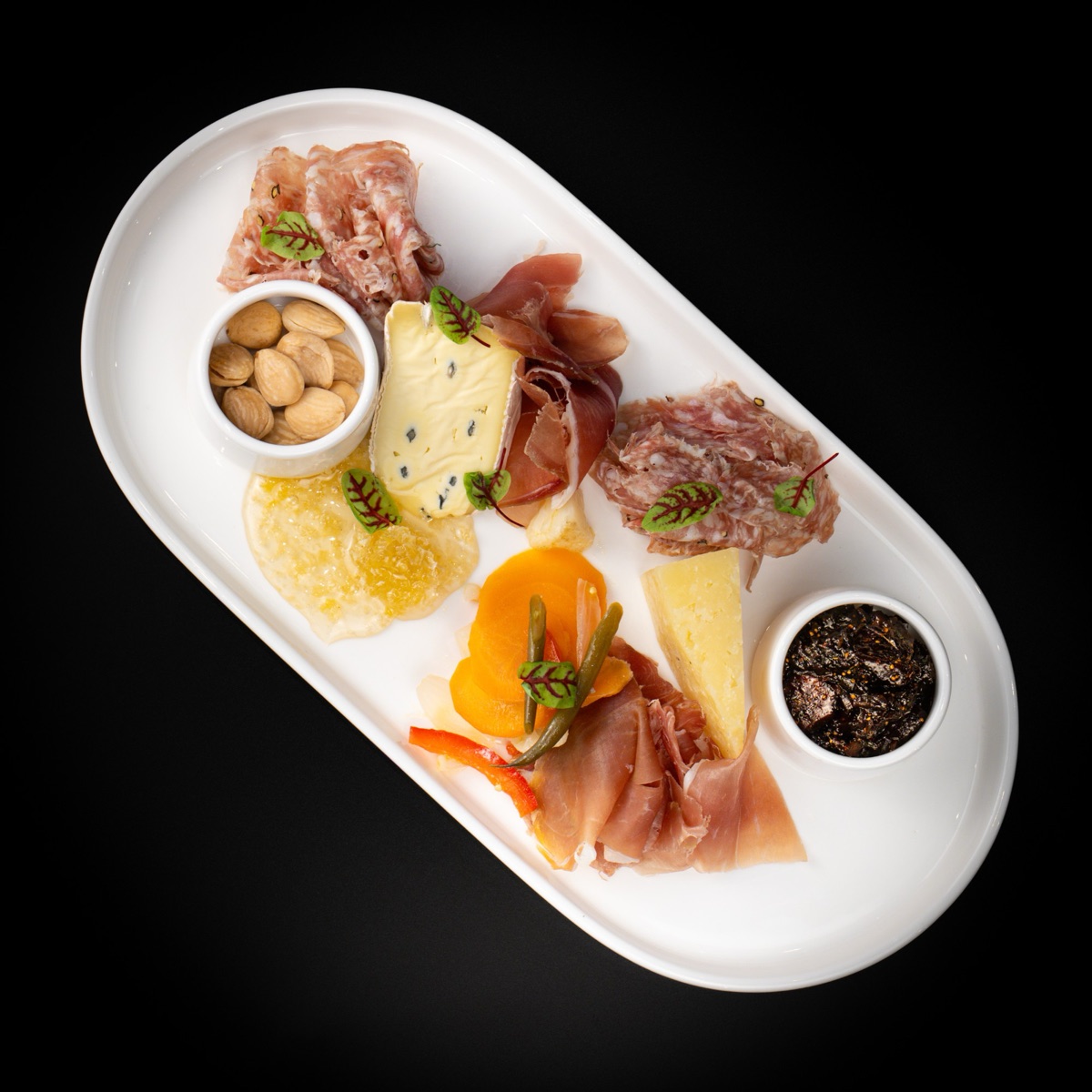 A charcuterie board with cured meats, cheeses, almonds, pickled vegetables and fig jam