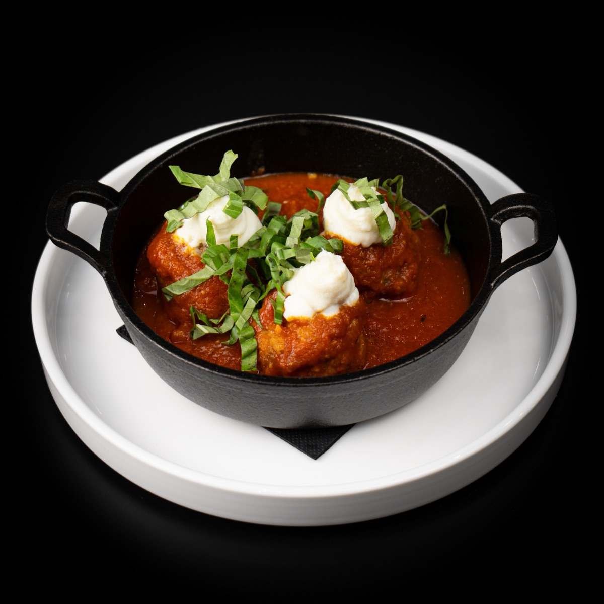 Meatballs in tomato sauce with ricotta and basil, served in a small cast-iron pot